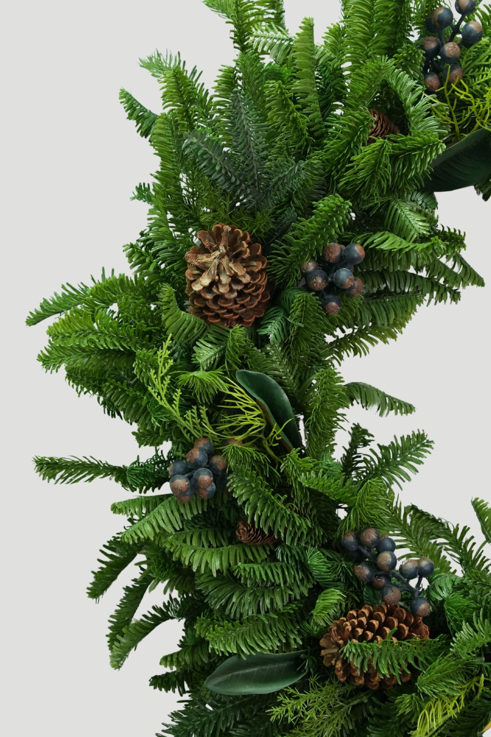 Close-up of mixed green needles, fine evergreen sprigs and blue berries on a Feel Real Christmas wreath