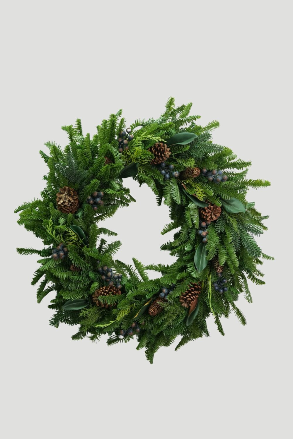 Full view of an 81cm Feel Real Mixed Evergreen Wreath with blue berries, magnolia leaves and pinecones