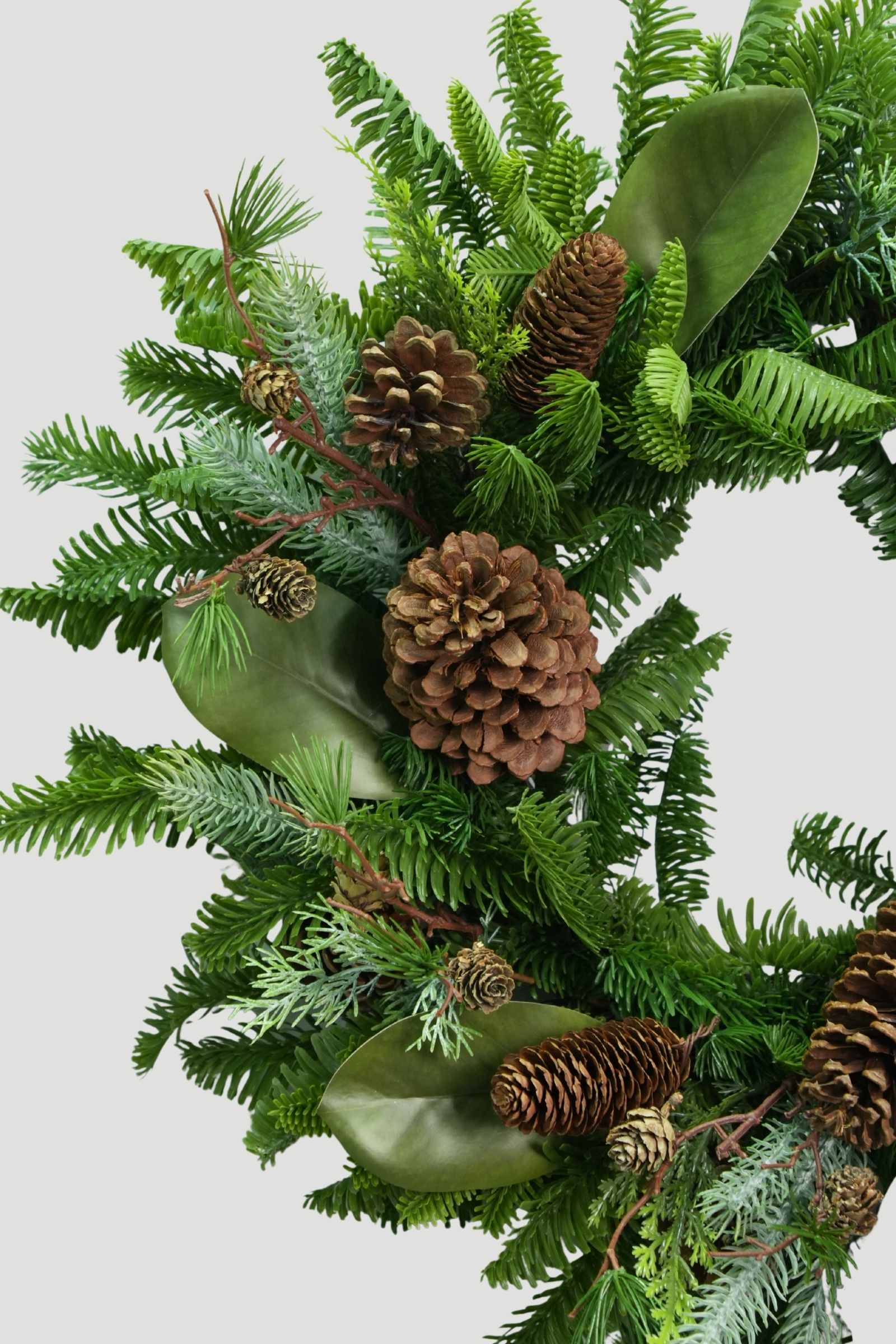 Close-up of green magnolia leaves, mixed evergreen foliage and brown pinecones on a Feel Real Christmas wreath