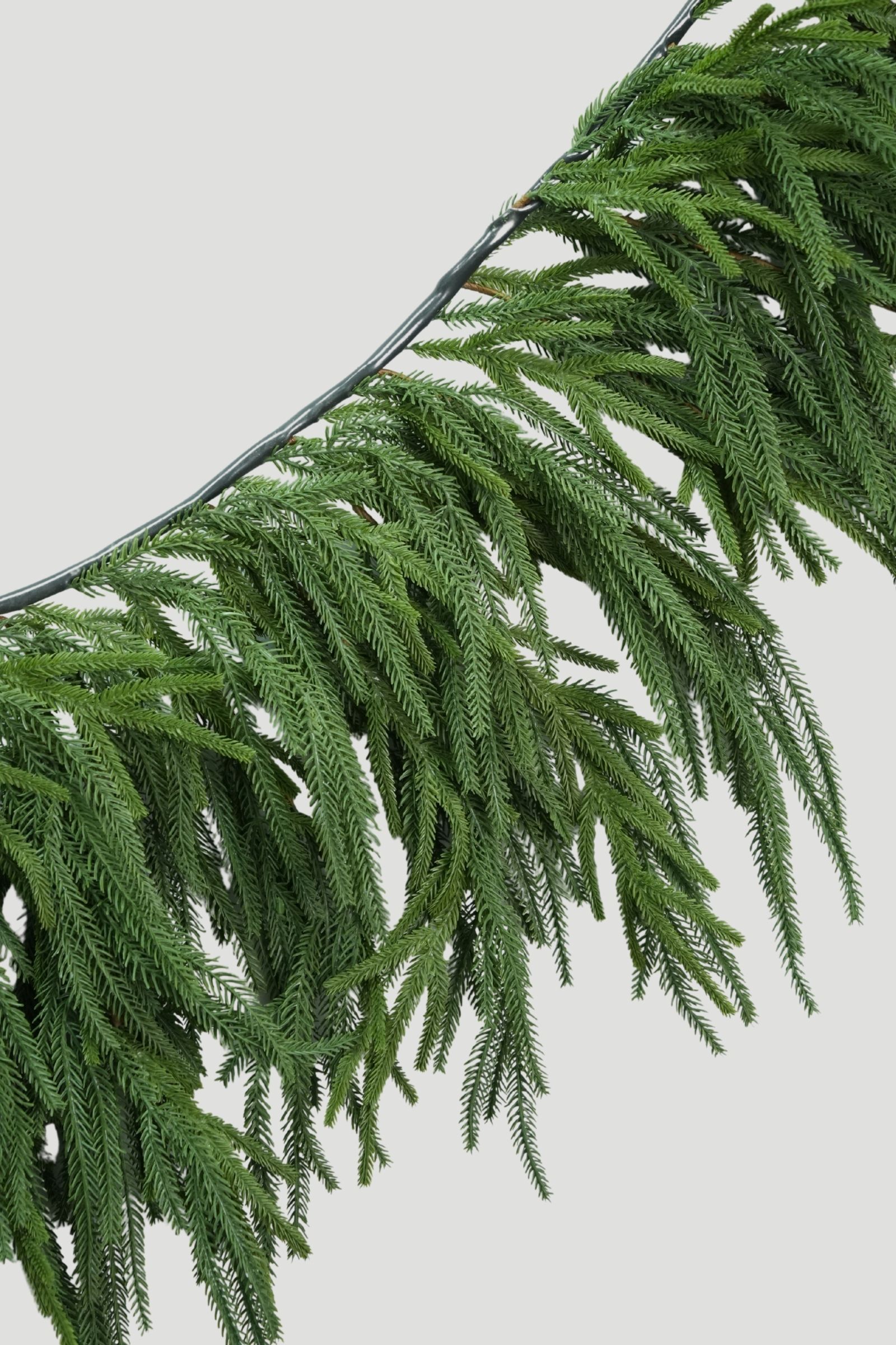 Close-up of long cascading green sprigs and finely textured needles on a Feel Real Norfolk Pine Mantel Garland