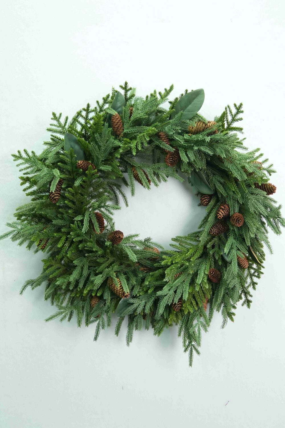 Vorderansicht eines Weihnachtskranzes aus Zedern- und Zypressenholz mit herabfließendem grünen Laub und braunen Tannenzapfen