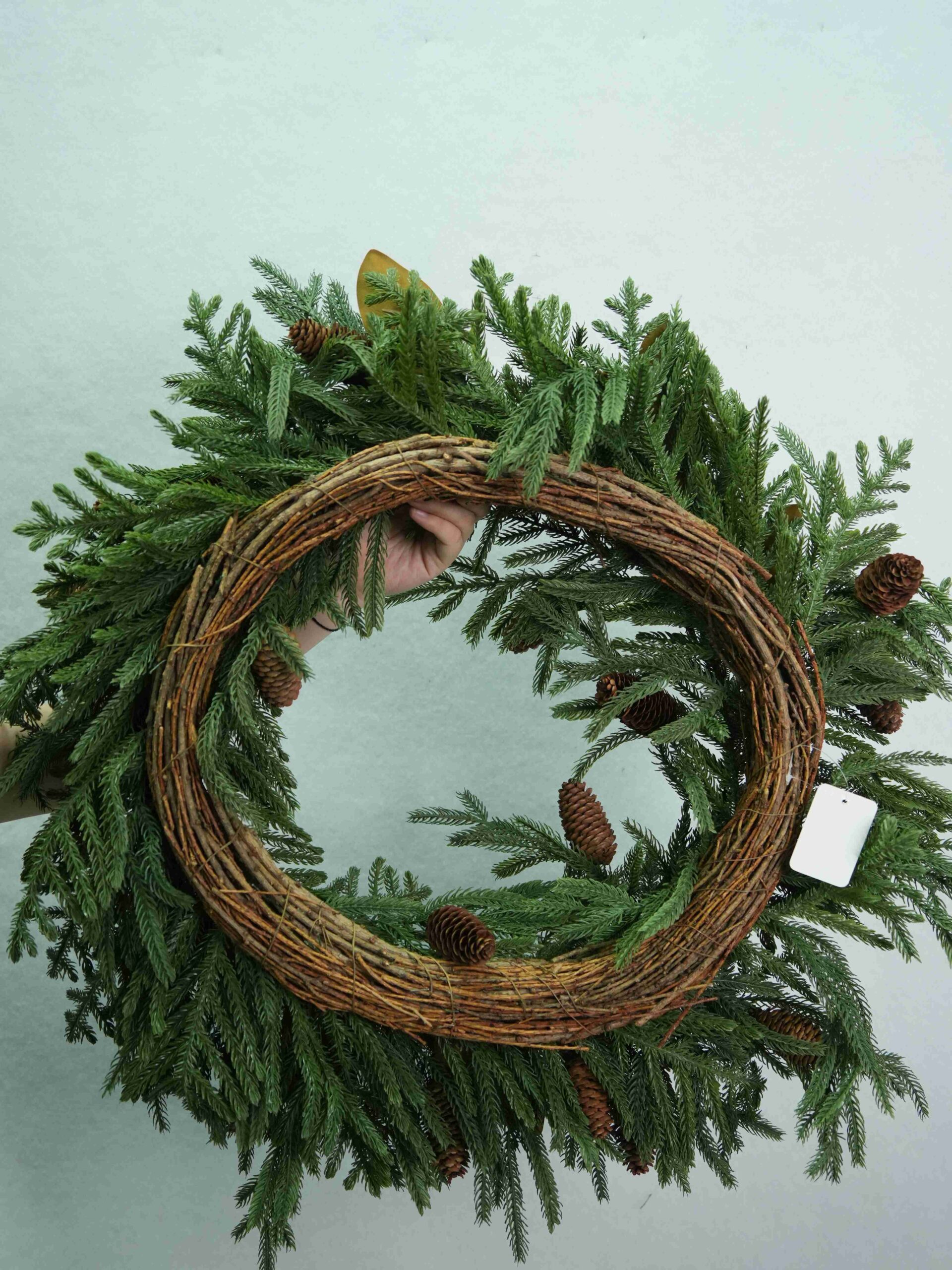 Rückansicht eines künstlichen Weihnachtskranzes mit kreisförmigem, gedrehtem Rankenfuß und umgebendem immergrünem Laub