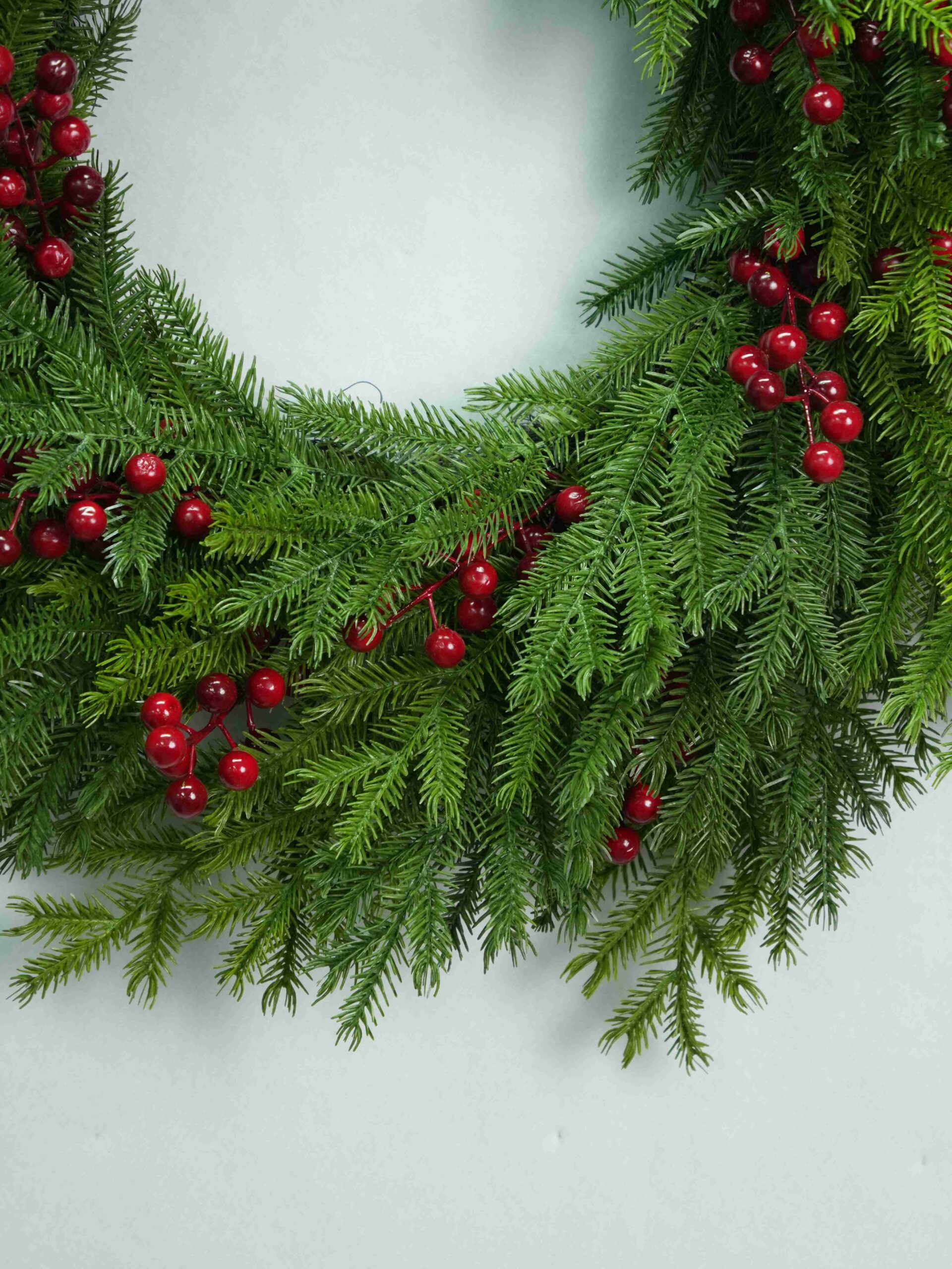 Nahaufnahme von roten Beeren, die zwischen übereinanderliegenden grünen Tannennadeln auf einem künstlichen Weihnachtskranz angeordnet sind